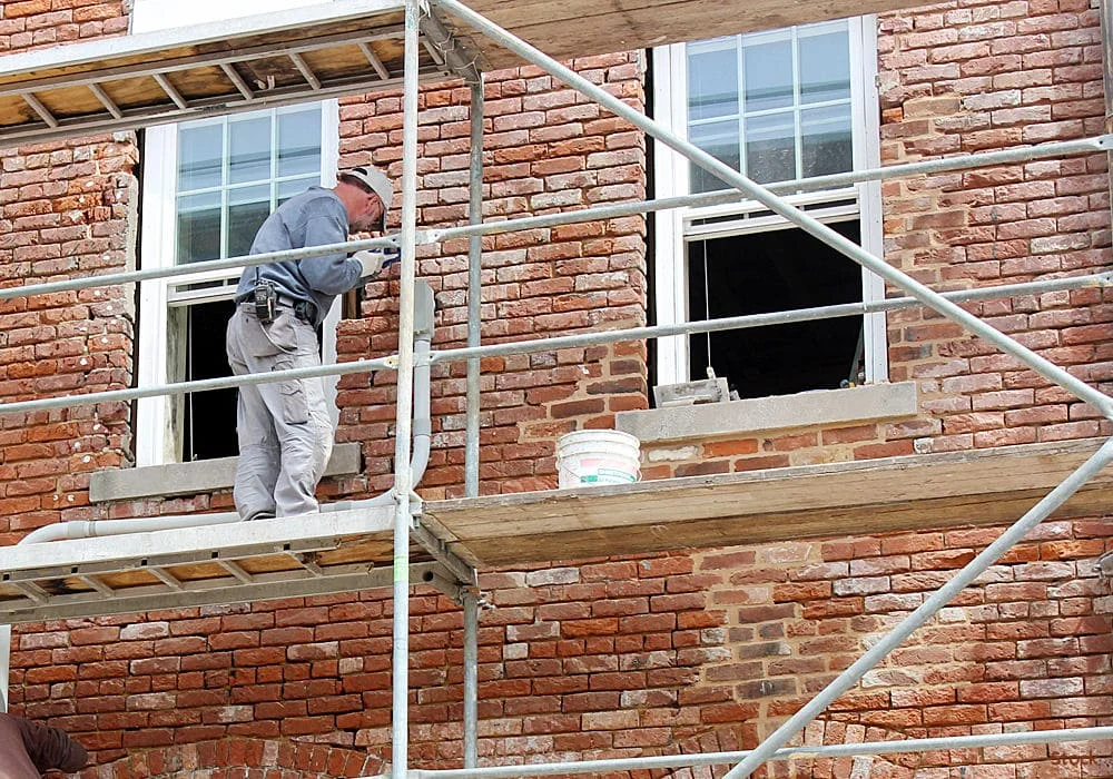 man-on-scaffold-tuckpointing-brick-wall-on-historic-building